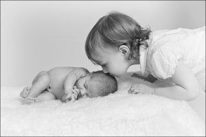 big sister kissing her newborn sister on the head
